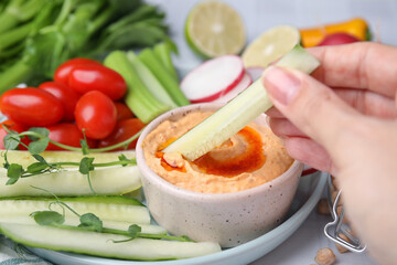Woman dipping cucumber stick into hummus at table, closeup