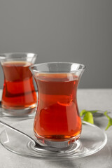 Glasses with traditional Turkish tea and green leaves on light grey table