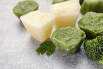 Frozen cauliflower and broccoli puree cubes on light grey table, closeup