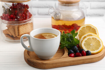 Cup with delicious immunity boosting tea and ingredients on white wooden table