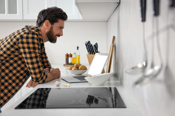 Man making dinner while watching online cooking course via laptop in kitchen