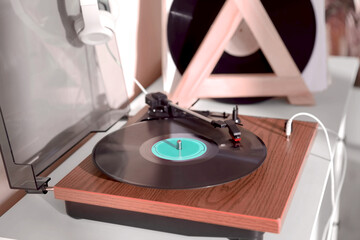 Stylish turntable with vinyl disc and headphones on white chest of drawers at home