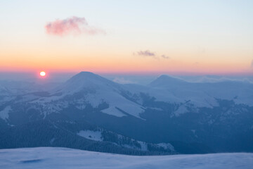 The sun disk rises above a snow-covered mountain at dawn. Petros and Hoverla Peaks