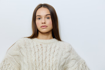 attractive, young woman stands in a white stylish sweater on a light background pleasantly looking at the camera with well-groomed hair