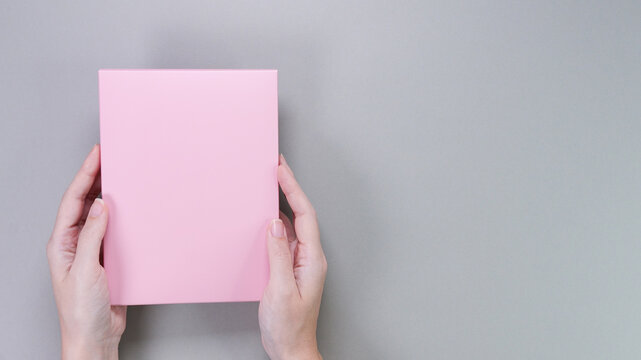 A square pink box with an copy empty space for text and design in the hand of a young woman in a white shirt on a pink background. Board, blank, template, mockup, layout for a slogan or inscription.