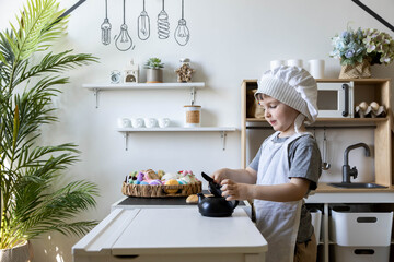 Cute little baby boy in chef hat and apron playing at childish kitchen cooking food back view