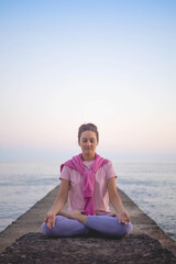 Fototapeta na wymiar Yoga woman meditation in lotus position at pebble sea beach sunset sky horizon healthy lifestyle