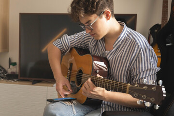Male teenager singing song playing acoustic guitar reading text on smartphone application screen