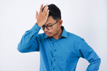Handsome young asian businessman with glasses in wearing blue shirt forgetting something, slapping forehead with palm isolated on white background