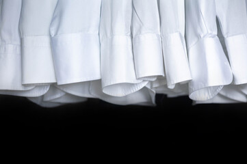 Male business wardrobe many clean white shirt sleeve hanging isolated on black background