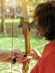 Female teacher teaches student to aim at goal. An archer teaching young man archery on field....