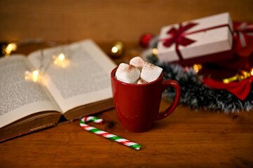 A cup of hot chocolate with marshmallow on wooden table with vintage book and Christmas decor - Powered by Adobe