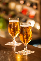 Two pints of lager beer standing on the bar table from a pub with bubbles coming out of the glasses. Photo with a scene from a bar. Beer beverages industry.