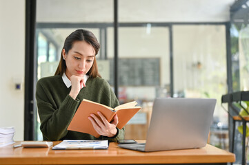 Determined Asian businesswoman reading a book, researching information in a textbook