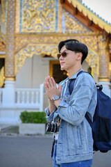 Handsome Asian male traveler putting his hands together in a prayer position in front of the temple