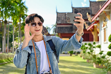 Handsome Asian male traveler taking selfie or making a video vlog with his smartphone