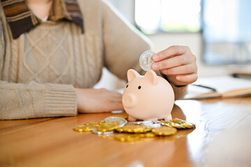 Obraz na płótnie Canvas A female insert coins into a piggybank. saving money and investment concept. cropped