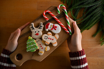A female's hands holding a wooden tray of gingerbreads and candy over wood tabletop