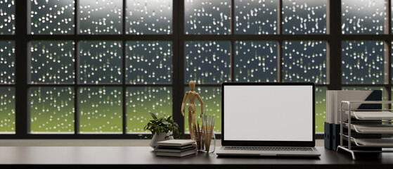 Office desk with laptop, office supplies on tabletop with raindrop on the window in background