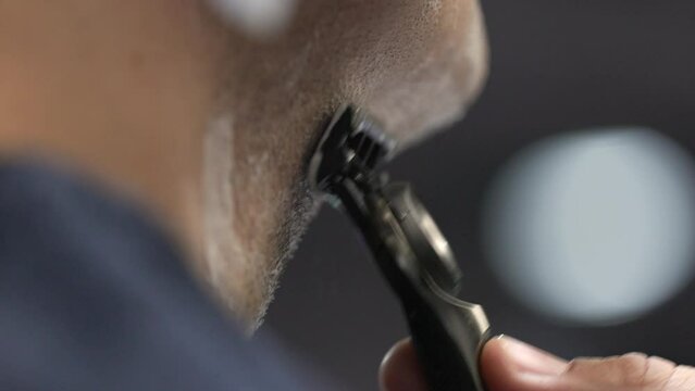 Close-up view of unrecognizable, caucasian man shaving his beard. Detailed shot of an adult male holding sharp razor blades during a morning routine procedure. High quality 4k footage