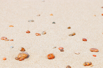 Fototapeta na wymiar Natural stones amber yellow colored on beige sand. Aesthetic minimal nature scene with pebble stones on fine sandy background. Summer vacation or relaxation concept, selective focus