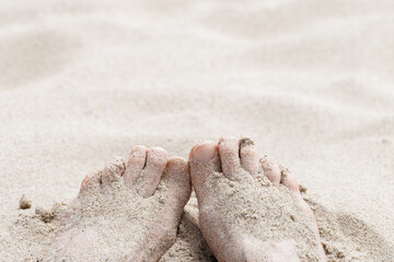 Summer rest or vacation on beach concept. Woman toes close up buried in sand on seashore. Female bare feet with natural toenails on white beige sand. Selective focus, blurred background