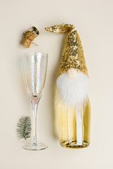 Champagne bottle decorated hat of dwarf with golden sequins, Christmas holiday and new Year party concept as festive still life pattern. Minimal trend beige flat lay, alcohol drinks, top view