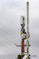Obraz premium Two linemen in a lift bucket installing new wireless technology, 5G antennas and electronics on top of a wooden glue laminate monopole 