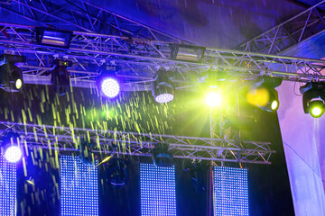 yellow and blue spotlights illuminate stage at a concert during the heavy rain