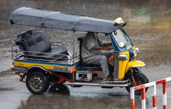 An empty Tuk Tuk motor tricycle is driving a city street in the rain, Thailand