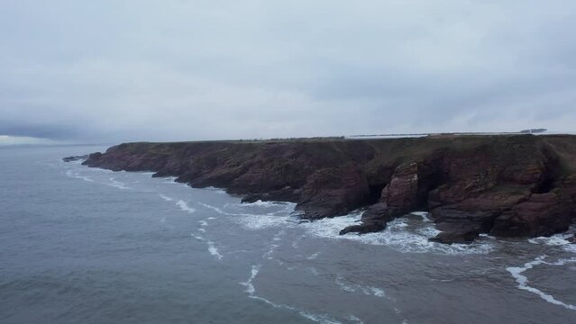 Drone shot of cliffs in Northern Scotland  on a grey day as the waves crash over them