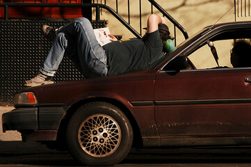 Obraz na płótnie Canvas a man reads a magazine sitting on the hood of a car