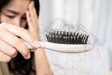 sad Asian woman have a problem with hair loss after brushing  holding a comb with hair fall
