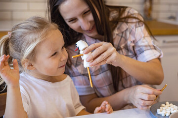 Mom and kids make snowmen from marshmallows. They drink cocoa and get ready for Christmas. Christmas home concept.