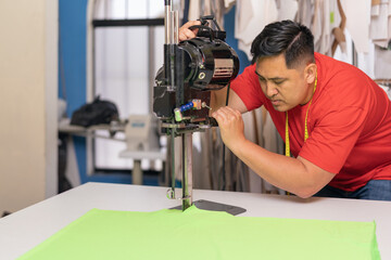 Concentrated man using a machine to cut clothes in a textile workshop