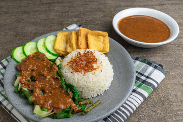 nasi pecel is traditional Indonesian javanese salad with peanut sauce. serve with steam rice, fried tofu, and cucumber