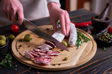 Woman slicing Spanish fuet salami sausageon wooden cutting board at domestic kitchen