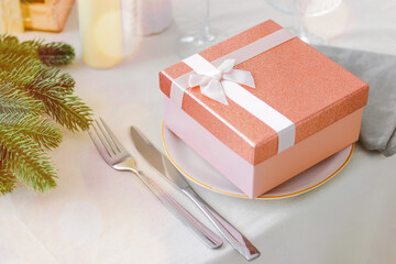 Festive table setting with a pink gift box in a plate on the table. Banner. Side view. Christmas or New Year concept.
