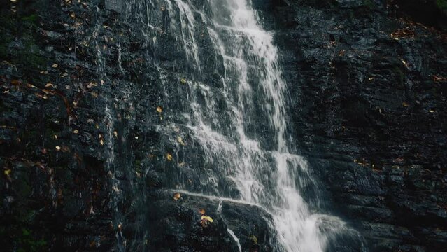 Close up of waterfall water splashing on dark mountain stones.