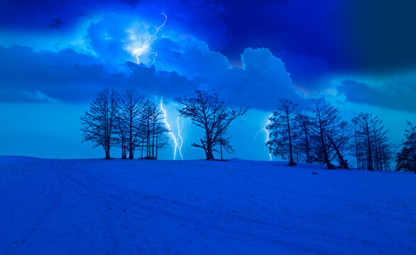 Beautiful winter landscape with dead trees and shadows on the snow lightning in the background