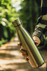Close-up of Unrecognizable female hand holding Water bottle. Reusable steel thermo water bottle in...