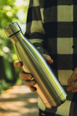 Close-up of Unrecognizable female hand holding Water bottle. Reusable steel thermo water bottle in...