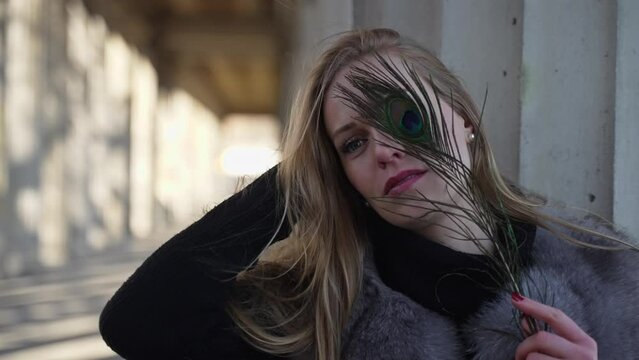 Blond Model Woman Posing for Photoshoot with Flashlight Outdoors Holding Peacock Feather Covering Face