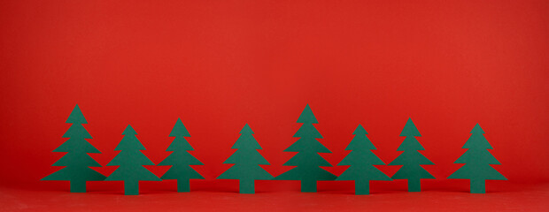 Red Christmas background with green paper spruces in row in modern minimal art cartoon style with...