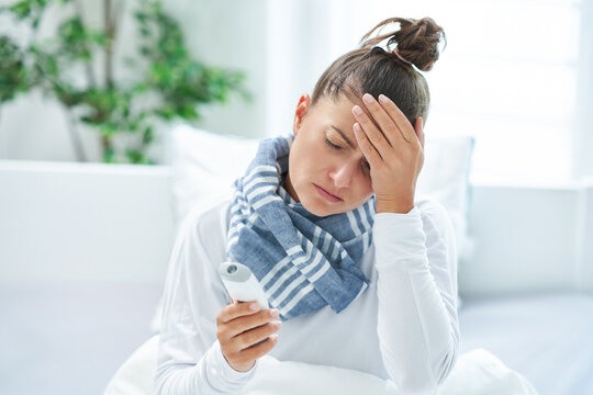 Young brunet woman sick in the bed with thermometer