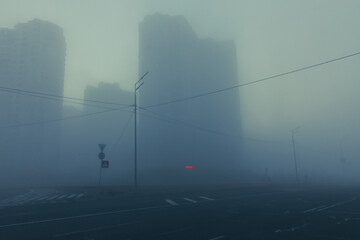 City street in the fog. Mysterious urban street with building silhouettes in the morning fog. Dream-like cityscape with an empty road.