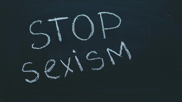 Close-up of a timelapse of a child's hand writing with chalk on a blackboard stop sexism. The concept of feminism, acceptance and women's rights