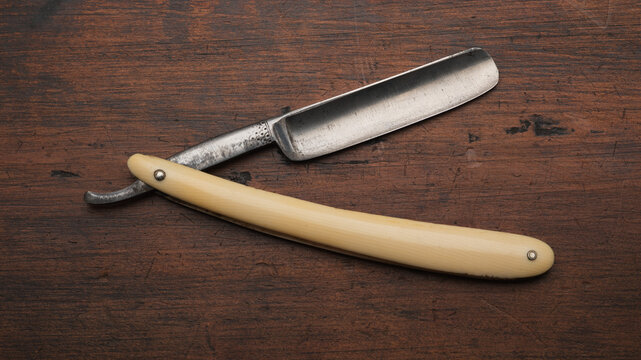 An old straight or cut throat razor overhead view lying on an aged wooden surface