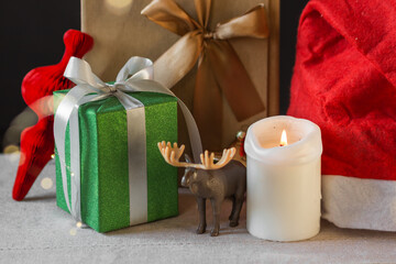 New Year or Christmas composition of wrapped gift boxes, toy deer, burning candle and Santa's hat. Garland bokeh light.