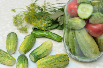 Cucumbers with green hot pepper on the table with glass jar with pickled vegetables cucumber and tomato with herbs and spices prepared for conservation. Selective focus. Harvest fall preparations 
